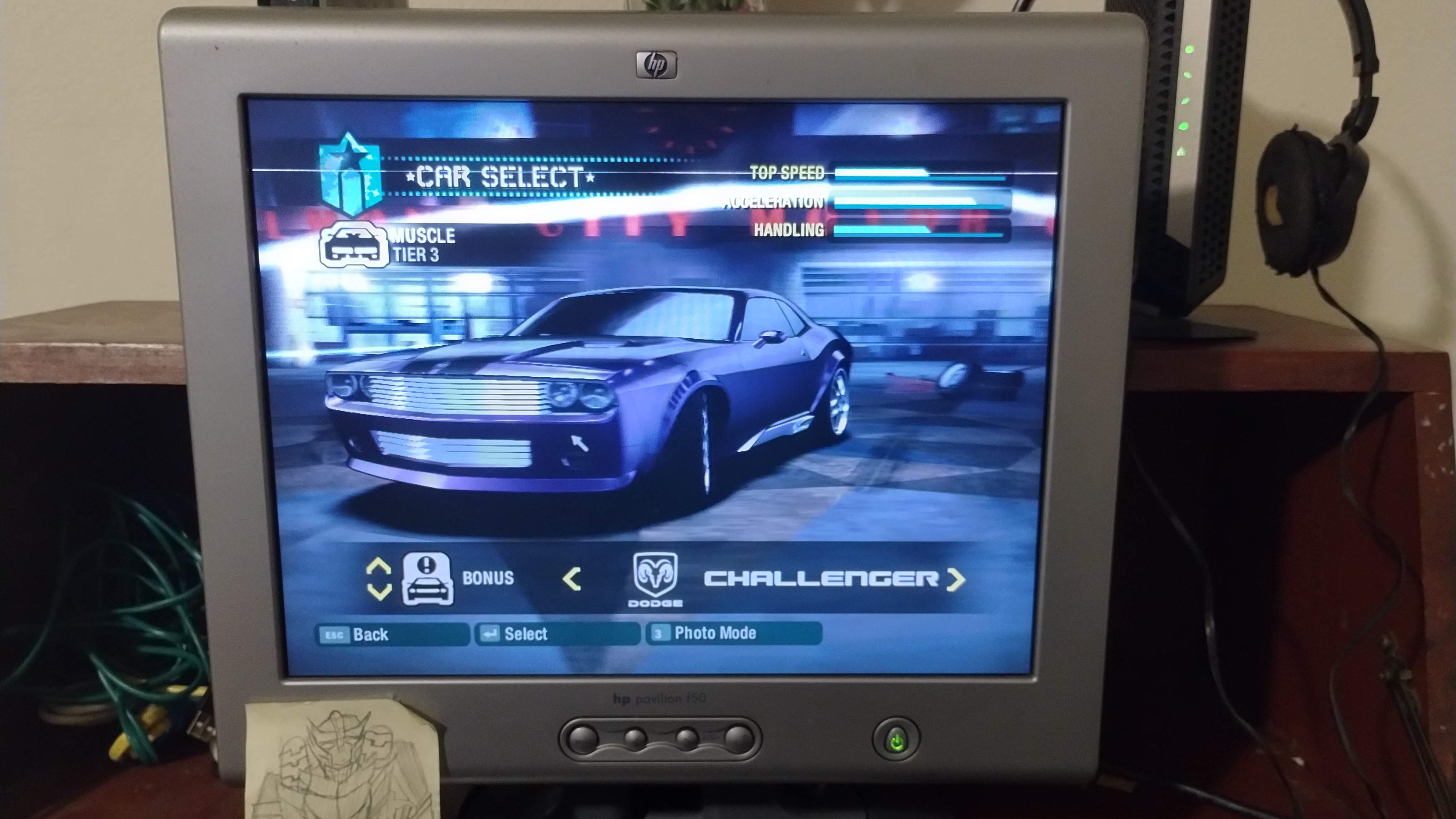 The vehicle selection screen of Need for Speed: Carbon. A dark purple 2000s Dodge Challenger has been selected and sits in the center of the screen in a dim garage.