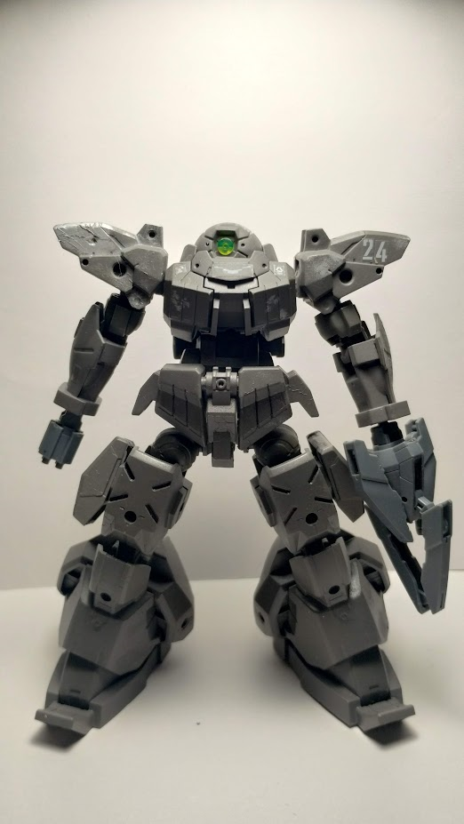 A painted model kit of a 30MM Revernova. The unit is dark gray with 24 on one shoulder and bare metal and chipping on the other. An arm mounted gatling gun has been affixed to the hand of the right, and a bulky claw to the left.