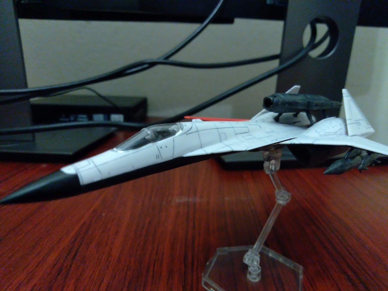 A model kit of a 1/144 ADFX-01 from Ace Combat Zero sitting on a desk. The angle has it facing forward at a 3/4 angle instead of top down.