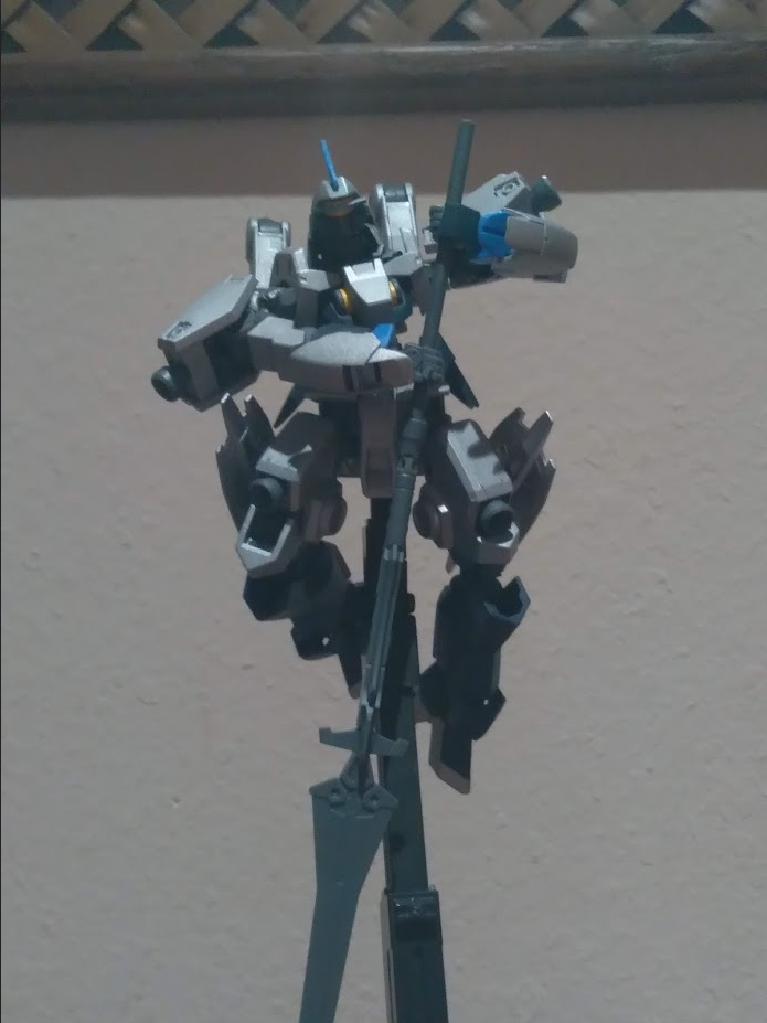 A model kit of a Schwalbe Graze from Gundam IBO mounted on a stand. The figure is posed holding a long spear pointed downwards.